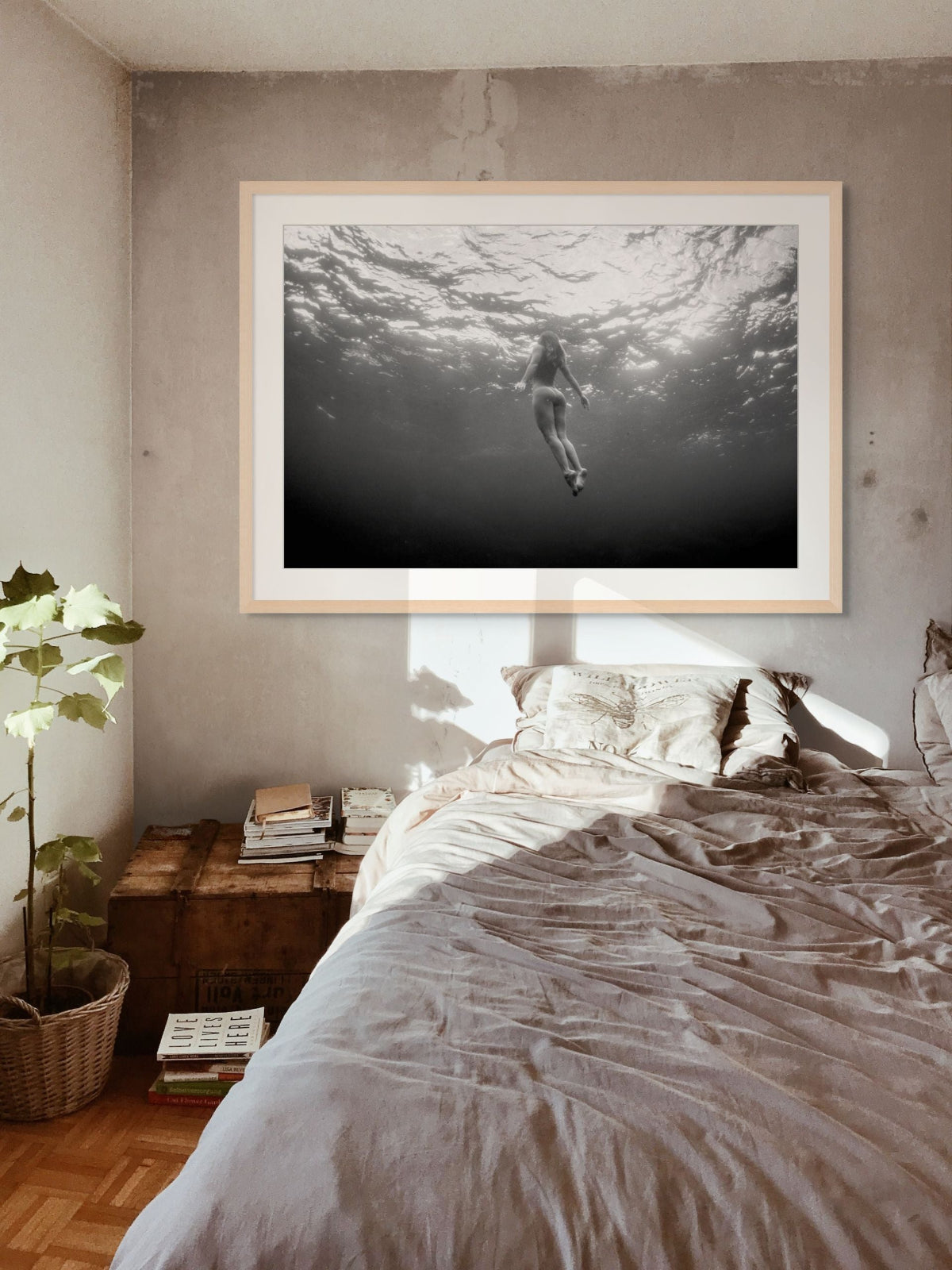 Framed black and white nude underwater fine art print above a bed in a bedroom.