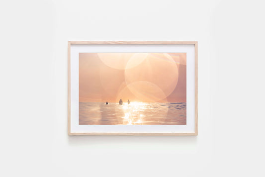 Framed Surfing print of a dreamy sunset over the ocean with surfers silhouetted in the warm light.