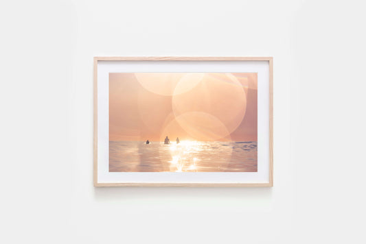 Framed Surfing print of a dreamy sunset over the ocean with surfers silhouetted in the warm light.