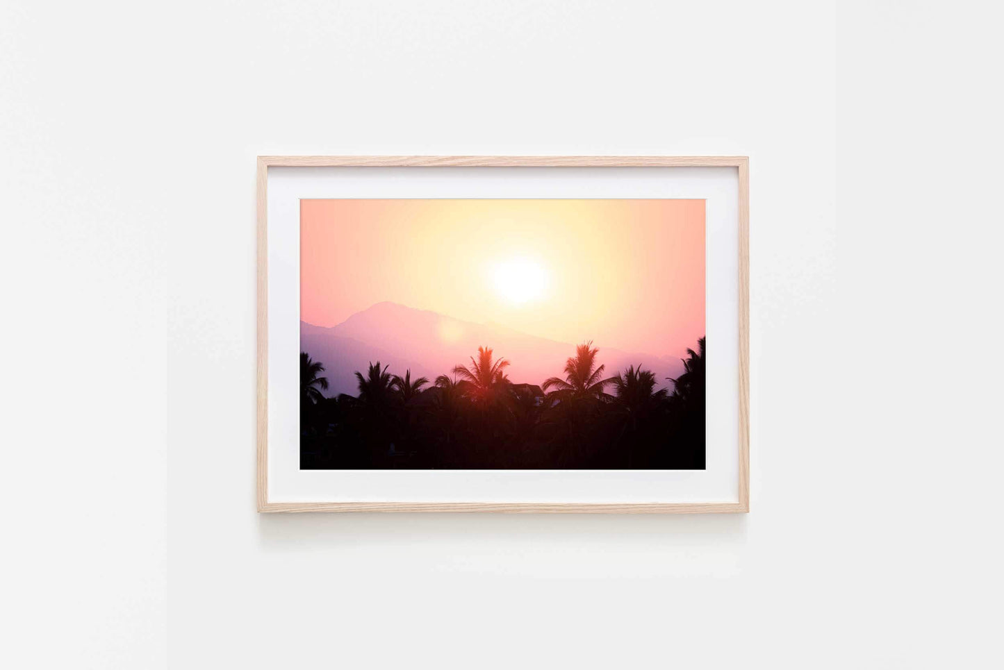 Image in natural timber frame of vivid sunrise colours over silhouette of palms and faint shapes of mountains in La Saladita, Mexico