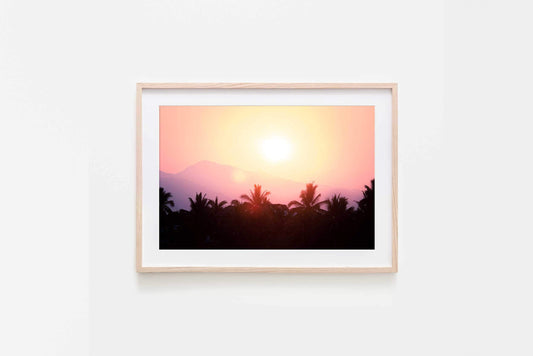 Image in natural timber frame of vivid sunrise colours over silhouette of palms and faint shapes of mountains in La Saladita, Mexico