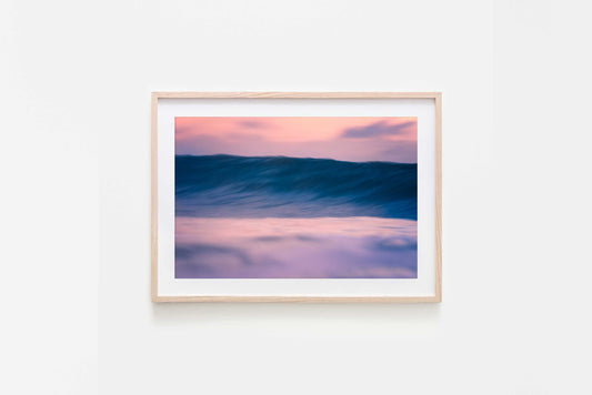 Framed artwork of a wave at sunset on a white wall