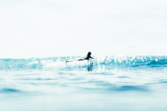 surfer paddling by in the ocean surrounded by sea sparkles and water textures