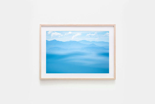 Blue mountain range with a hazy effect and a clear sky image in a natural timber frame with white matte board