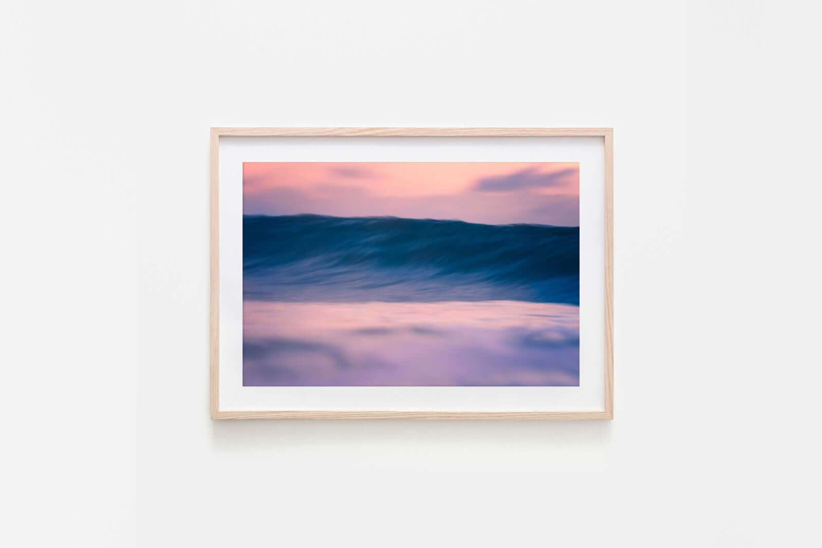 Framed artwork of a wave at sunset on a white wall