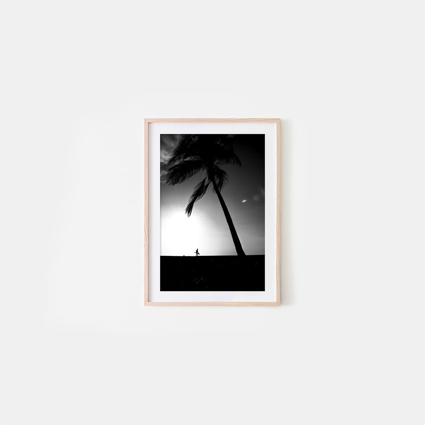Framed black and white artwork of palm trees and a person on a beach against a sunset sky.