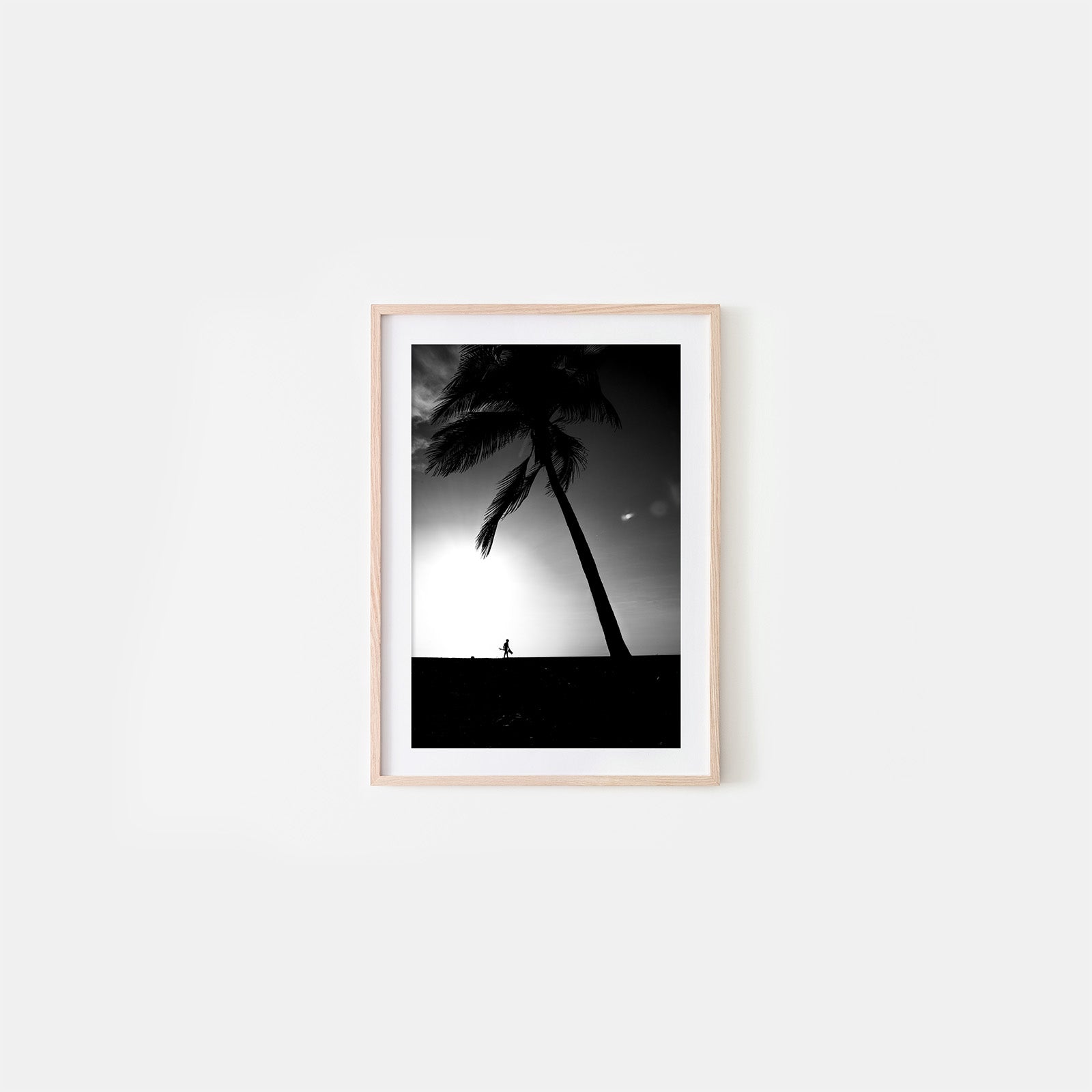 Framed black and white artwork of palm trees and a person on a beach against a sunset sky.