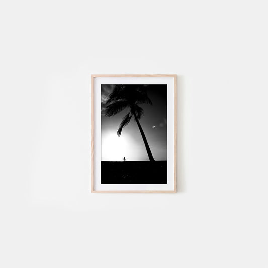 Framed black and white artwork of palm trees and a person on a beach against a sunset sky.